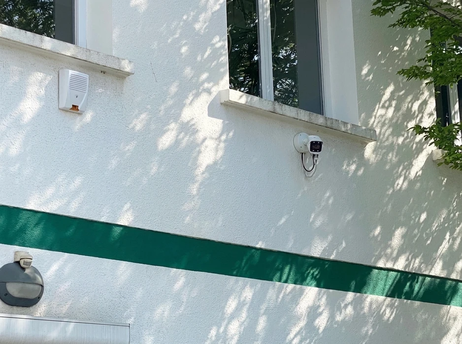 Façade extérieure blanche avec bande verte horizontale, équipée d'un système de sécurité complet