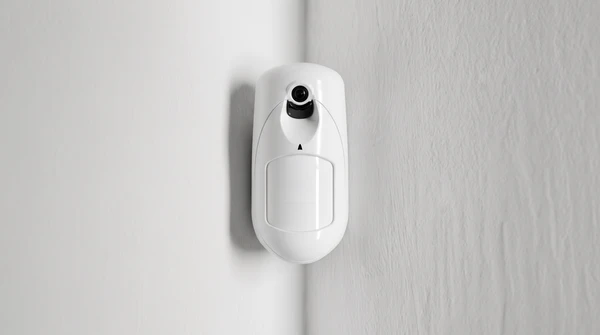 Intérieur résidentiel avec détecteur de mouvement PIR blanc monté au plafond dans l'angle d'une pièce aux murs blancs